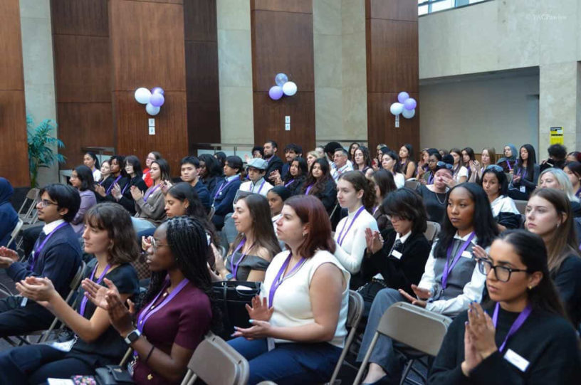 Photo of a crowd sitting while clapping at a Pen For Justice event