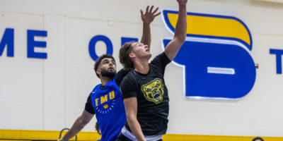 Oakland player jumps and drives toward net while TMU defender guards from behind