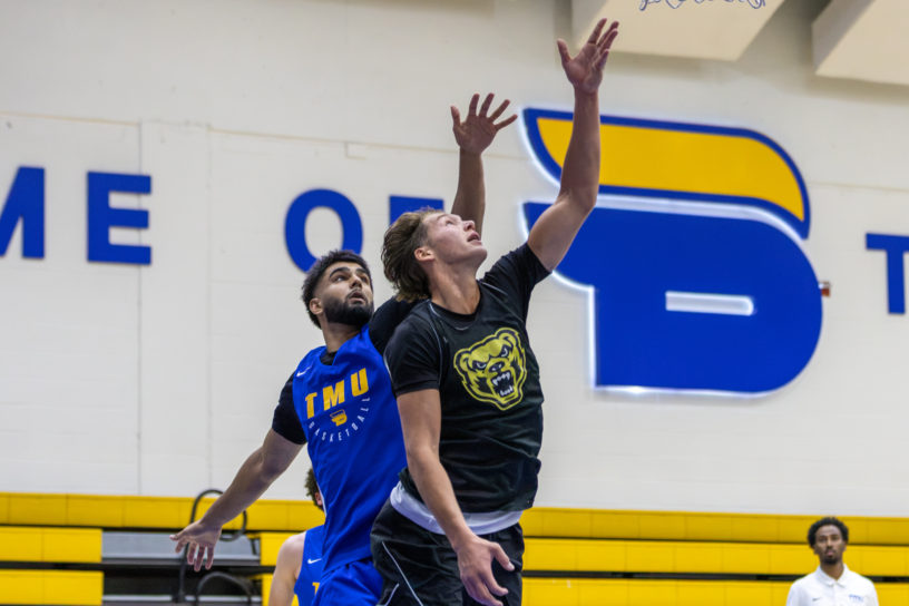 Oakland player jumps and drives toward net while TMU defender guards from behind
