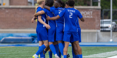 TMU Bold men's soccer team embrace on the pitch.