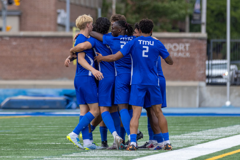 TMU Bold men's soccer team embrace on the pitch.