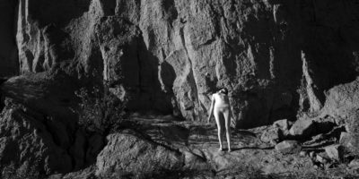 A black and white photo of a woman alongside a rocky surface.