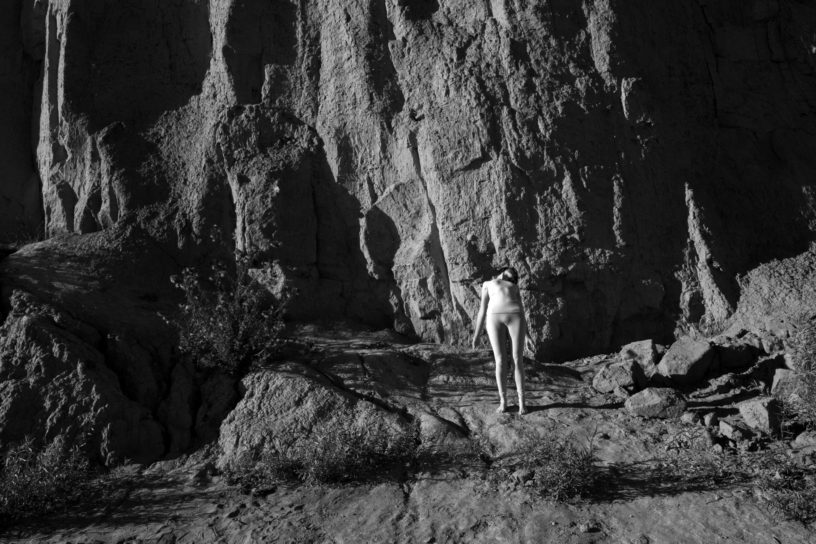 A black and white photo of a woman alongside a rocky surface.