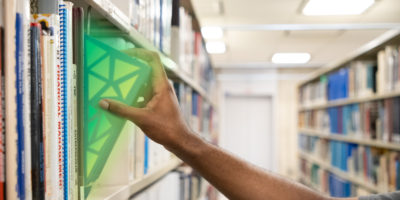 Student grabbing a book in a library, it glows green like a hidden gem.