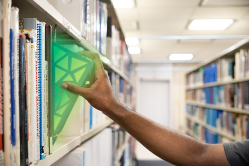 Student grabbing a book in a library, it glows green like a hidden gem.