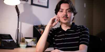 Photo of Edward Lander sitting at a desk with one hand on the table and one on his face.