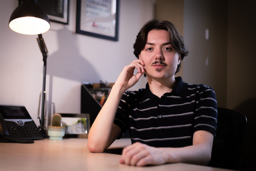 Photo of Edward Lander sitting at a desk with one hand on the table and one on his face.