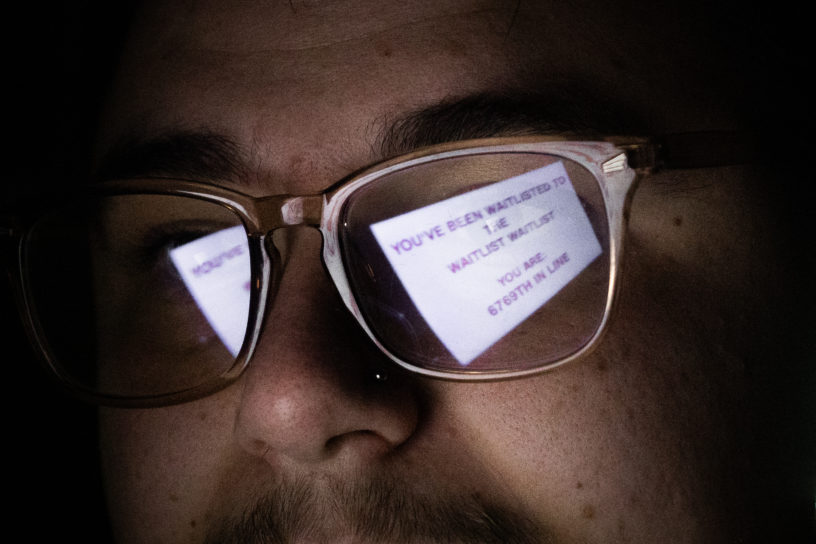 Photo of a man wearing glasses with the reflection of the glasses reading: "YOU'VE BEEN WAITLISTED TO THE WAITLIST WAITLIST" "YOU ARE: 6769TH IN LINE".
