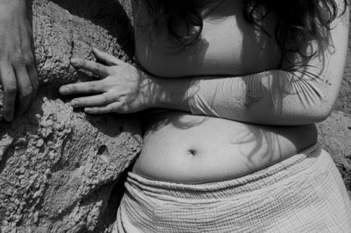 A black and white close up image of a person's torso. They are holding onto the rock face beside them.