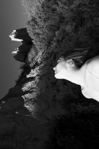 A black and white image of a woman's side profile, which mirrors the shape of the clifftop behind her.