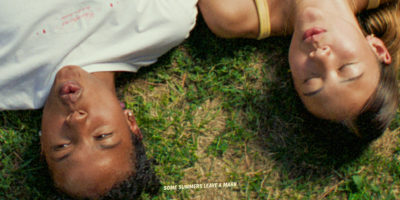 A still from the movie Sunburn. Two women laying in the grass, with a line of text reading "Some summers leave a mark."