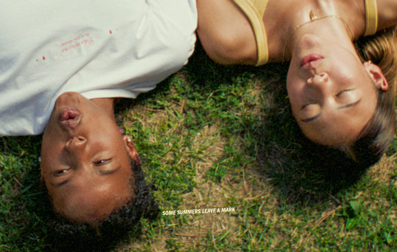 A still from the movie Sunburn. Two women laying in the grass, with a line of text reading "Some summers leave a mark."