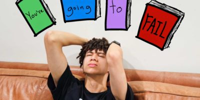 Image of someone appearing to be distraught, with four textbooks reading out "You're" "going" "to" "FAIL".