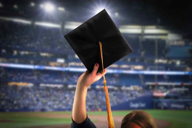 Photo of someone holding up a graduation cap on a background of a packed Rogers Centre.