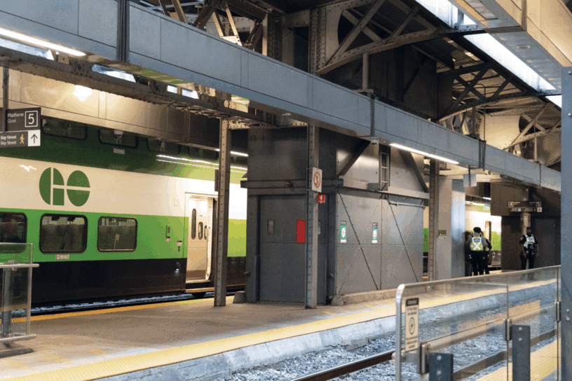 A GoTrain platform with a train on it, and some security guards standing on the platform in neon vests.