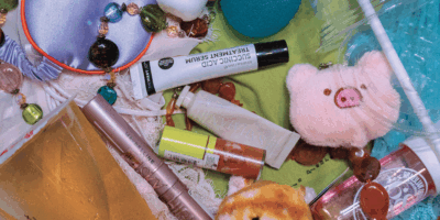 Picture of various colourful skin care, makeup, plushie, and food items on top of a background of green, blue and pink clothes.