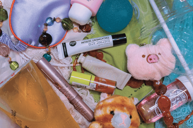 Picture of various colourful skin care, makeup, plushie, and food items on top of a background of green, blue and pink clothes.
