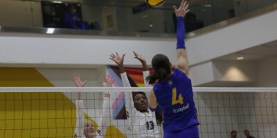 A Lakehead volleyball player attempts a kill in front of two TMU blockers