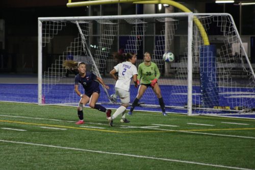 TMU and U of T player eyeing a soccer ball in front of the U of T net