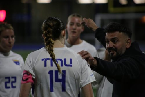 TMU head coach John Yacou talking to third-year midfielder Natalie Moynihan as fourth year midfielder Becca Bartosh stands in the background