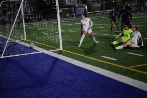 TMU goalkeeper and player watch as a soccer ball rolls into the TMU net