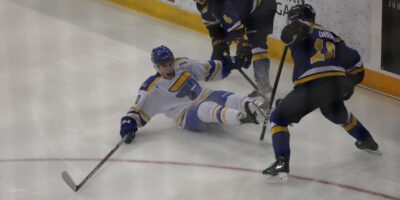 hockey player falls on ice surrounded by two opponents