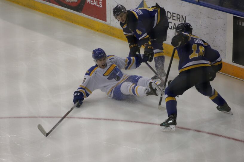 hockey player falls on ice surrounded by two opponents