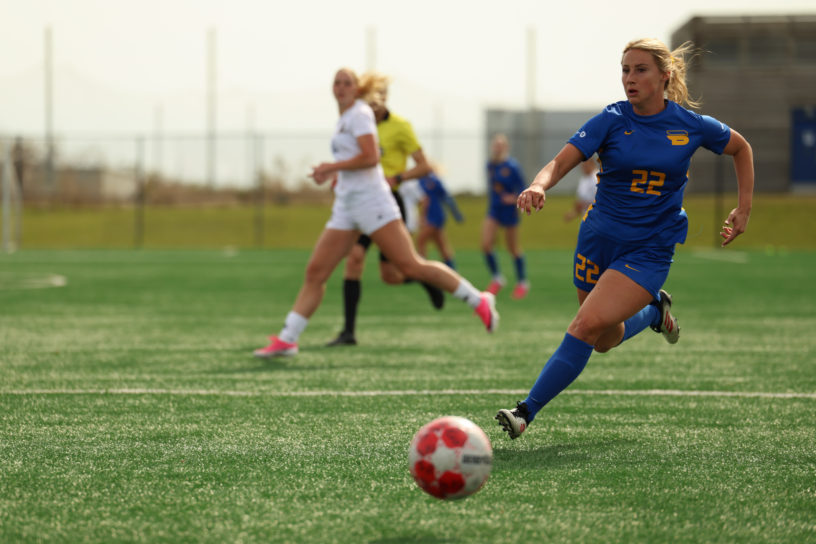 Soccer player chasing ball on pitch