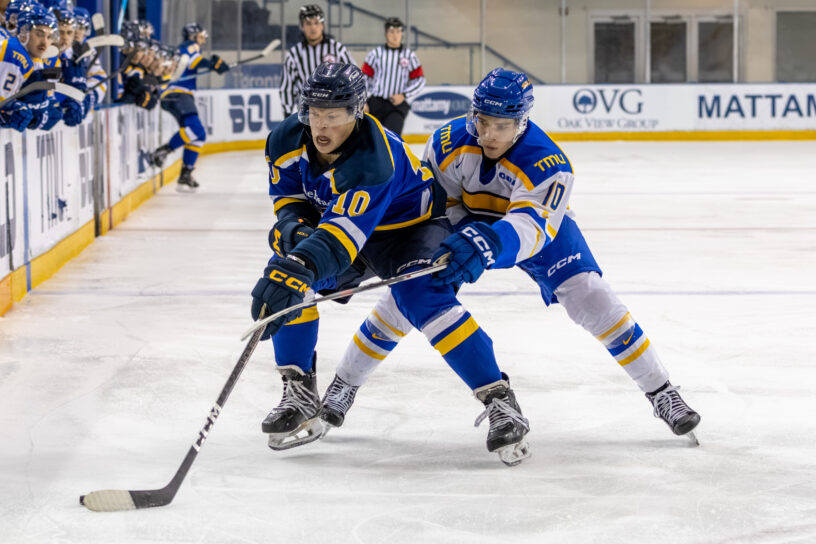 A TMU and a Lakehead hockey player fighting for the puck