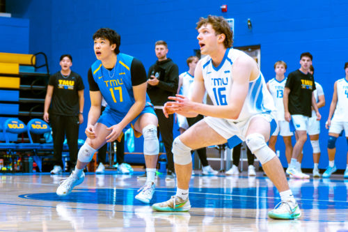 Two TMU volleyball players prepare to receive the ball