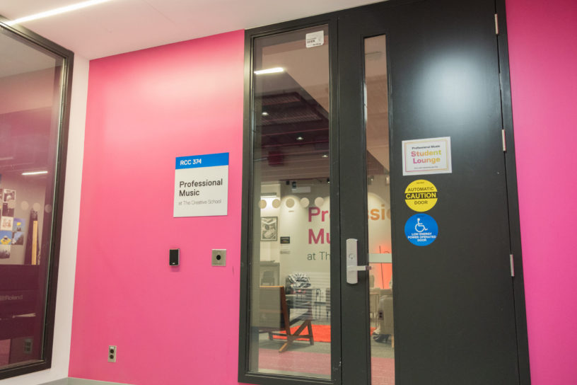 Image of the outside of a room with a pink wall with a sign titled "professional music student lounge"