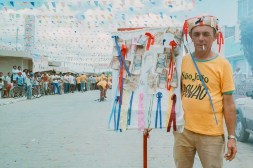 Photo of a man holding a sign with various ribbons and Brazilian reais.