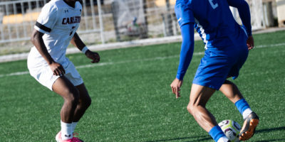 Two people playing soccer, one wearing a "Carleton" and "TMU" jersey.