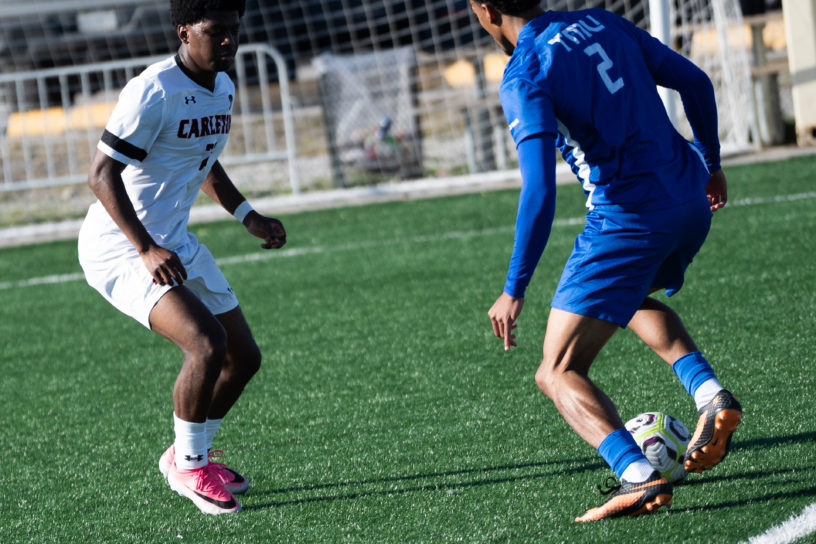 Two people playing soccer, one wearing a "Carleton" and "TMU" jersey.