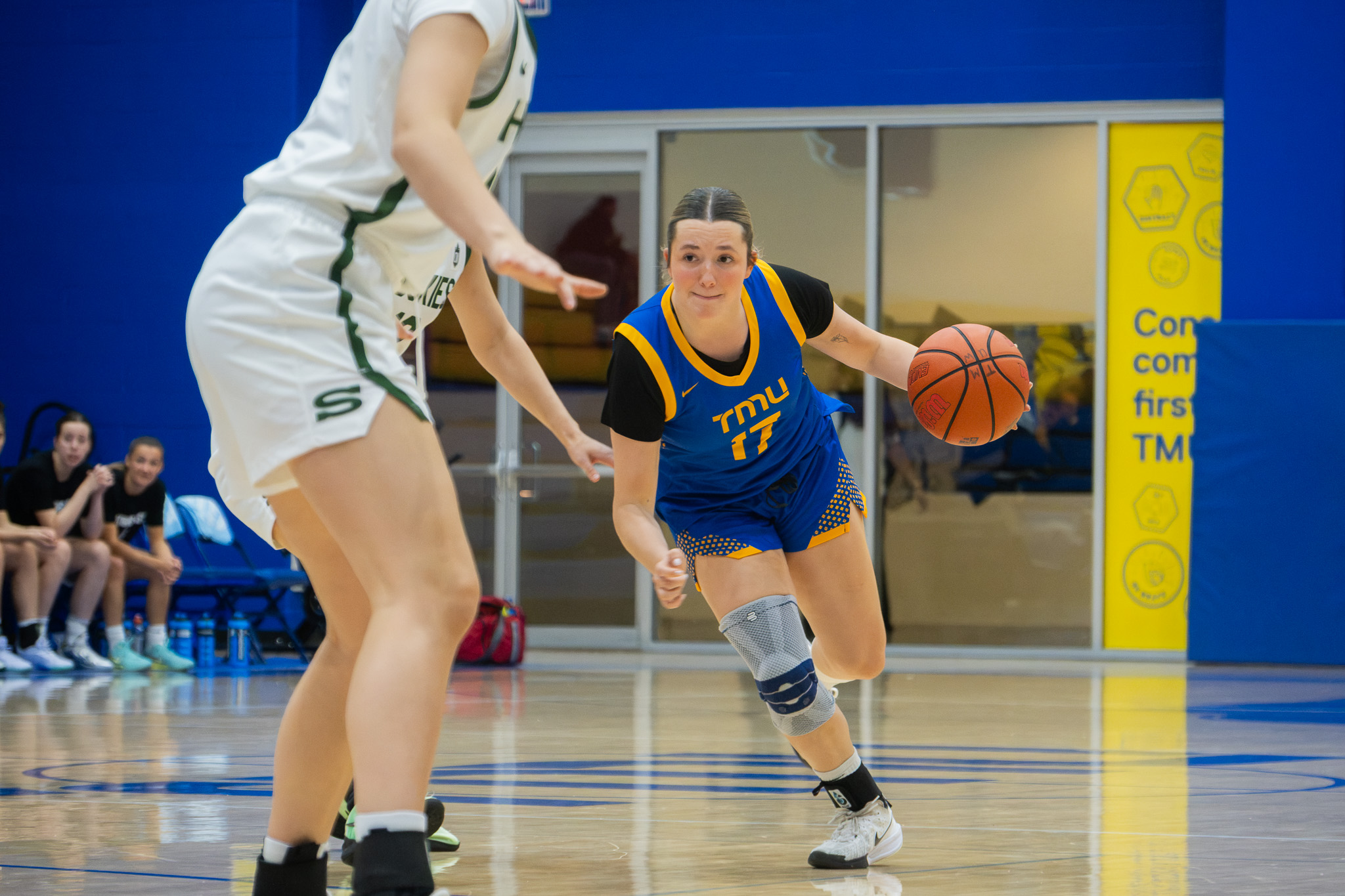TMU player dribbles in the background in front of a Saskatchewan player