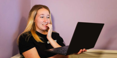 A girl looks on her computer and bites her nails nervously.