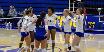 The TMU women's volleyball team celebrates in a circle on court
