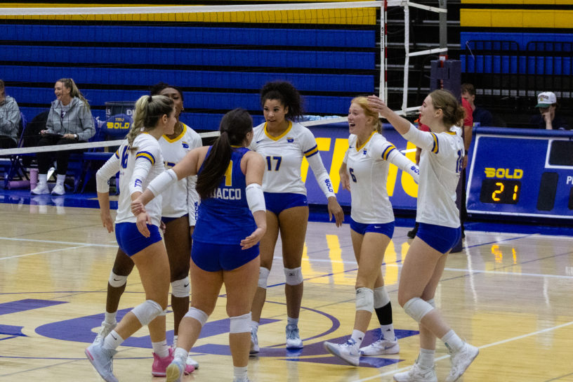 The TMU women's volleyball team celebrates in a circle on court