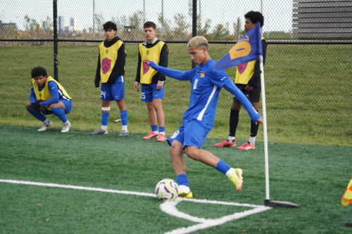 Bold soccer player takes a corner kick in the foreground as four Bold players watch on in the background