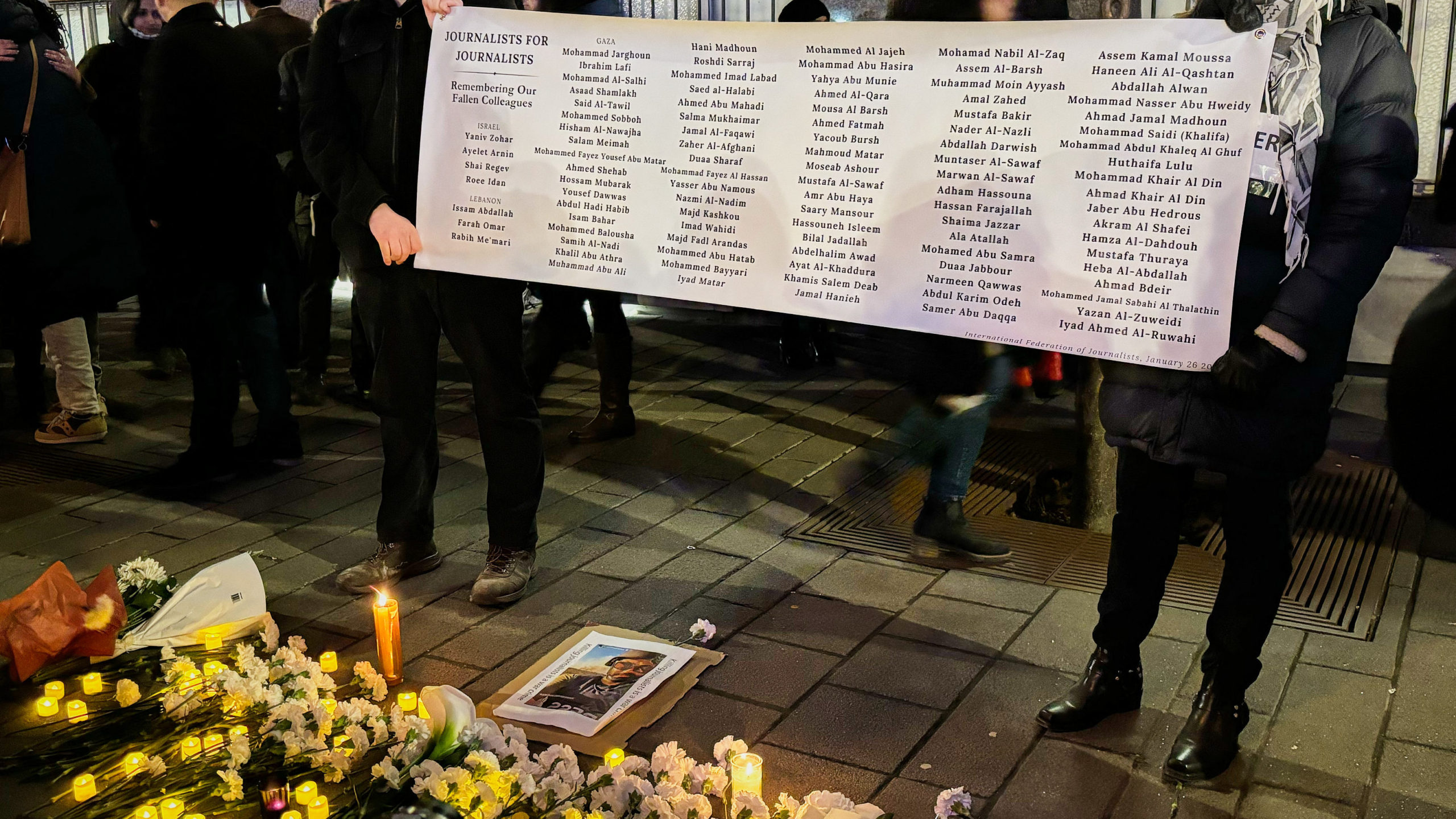 a poster with names is held up by two people at a vigil
