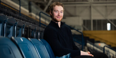 Photo of a person sitting in bleachers while looking at the camera.