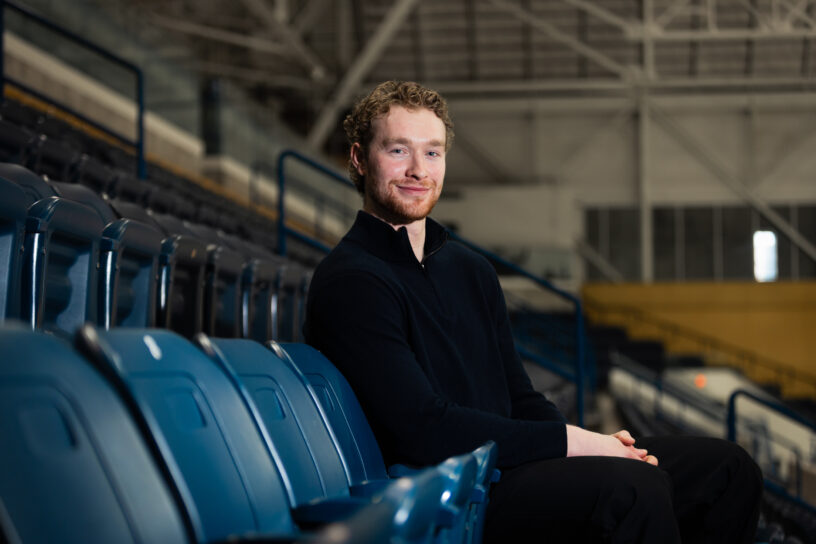 Photo of a person sitting in bleachers while looking at the camera.